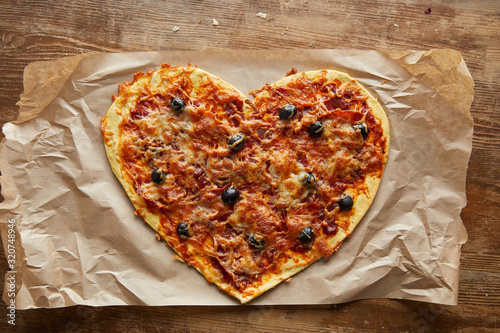top view of delicious italian pizza in heart shape on baking paper on wooden table
