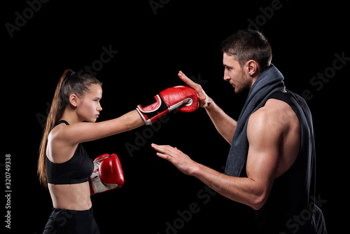 Young sportswoman in activewear and boxing gloves exercising with trainer consulting her about rules of fight