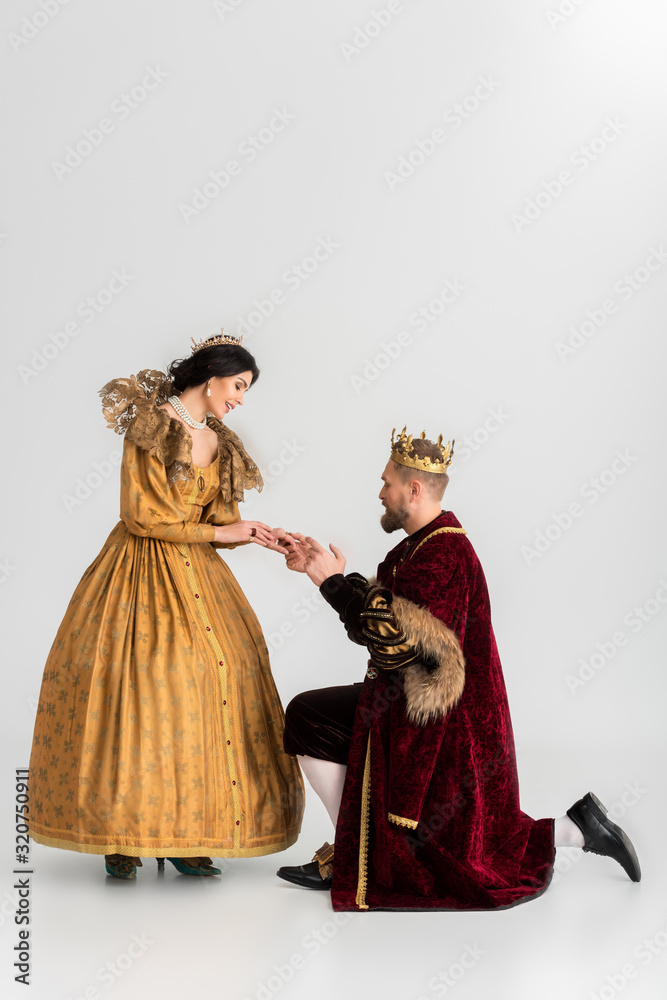 smiling queen and king with crowns holding hands on grey background