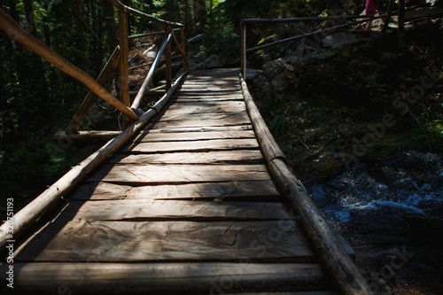 Fototapeta Naklejka Na Ścianę i Meble -  Wooden bridge with steps on the eco-trail along the rocks and mountain river in Bulgaria, Smolyan city. Equipped tourist road through the forest for sightseeing tours and walks