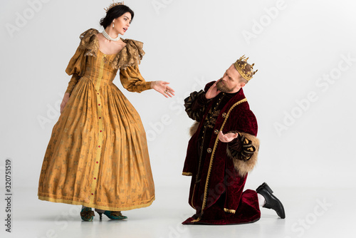 queen talking and king with crown bending on knees on grey background