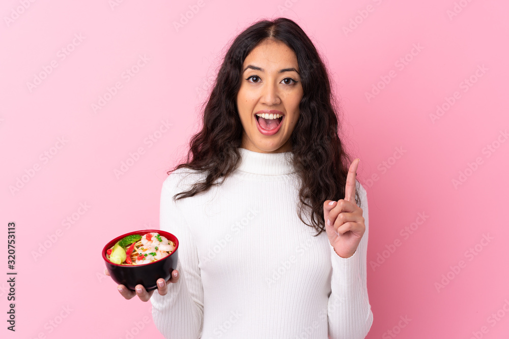Mixed race woman holding a bowl full of noodles over isolated pink background pointing up a great idea Mixed race woman holding a bowl full of noodles over isolated pink background pointing up a great idea