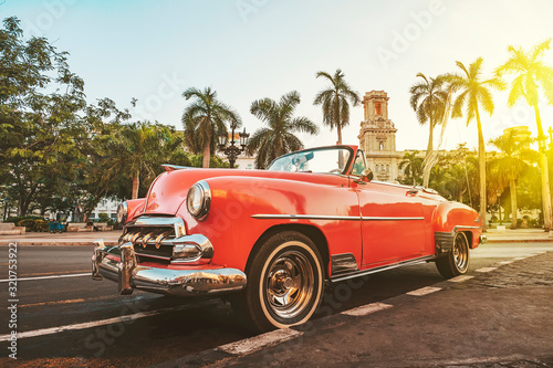 Classic American car against the background of palm trees in bright sun in the evening in Havana against the background of colonial architecture