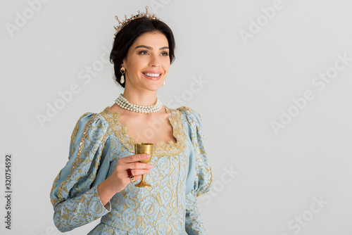 smiling queen with crown holding cup isolated on grey