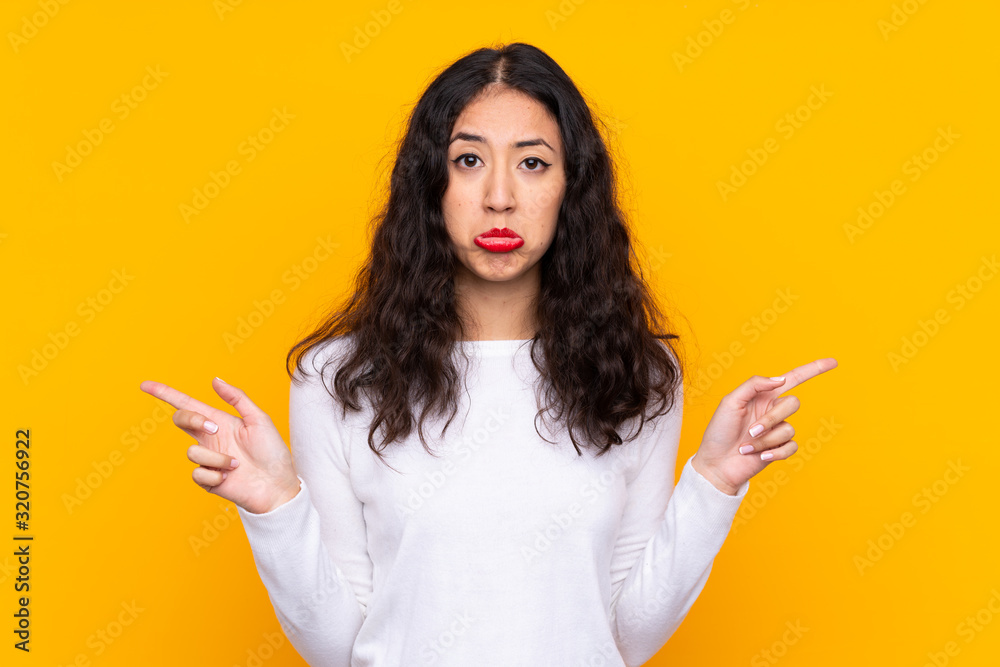 Mixed race woman over isolated yellow background pointing to the laterals having doubts
