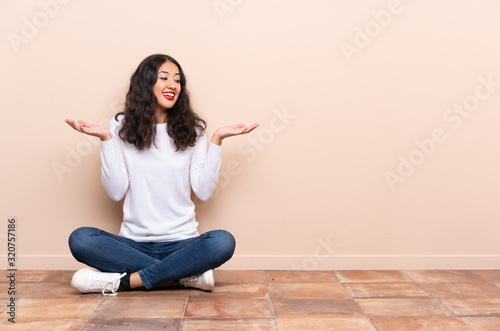 Young woman sitting on the floor holding copyspace with two hands
