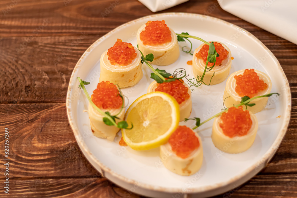 Dough rolls with cheese, red caviar. Garnished with sprigs of microgreen, a slice of lemon. On a wooden natural background. Dough rolls with cheese, red caviar. Garnished with sprigs of microgreen, a slice of lemon. On a wooden natural background.