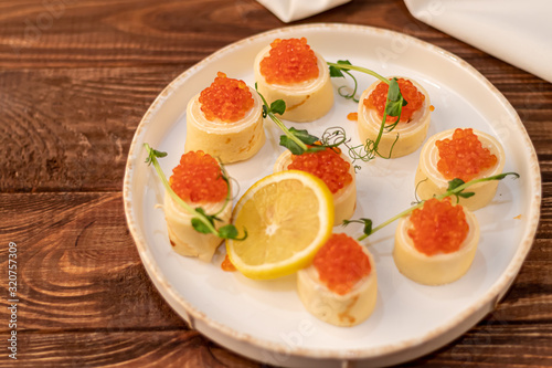 Dough rolls with cheese, red caviar. Garnished with sprigs of microgreen, a slice of lemon. On a wooden natural background.