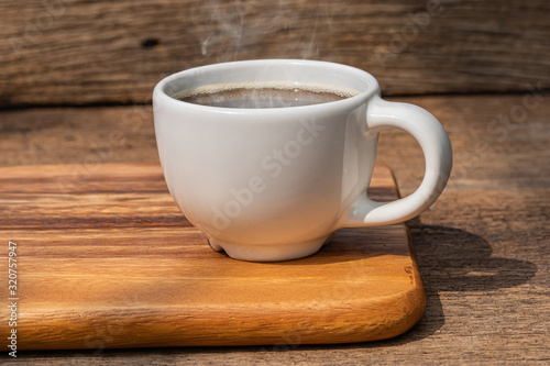 A white cup of hot coffee on wooden background.