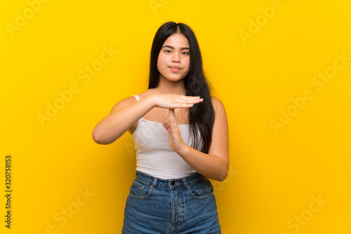 Young teenager Asian girl over isolated yellow background making time out gesture