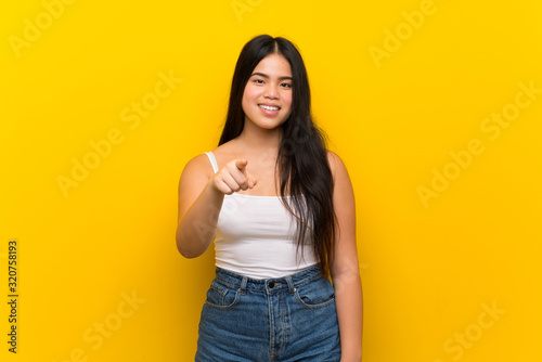 Young teenager Asian girl over isolated yellow background surprised and pointing front