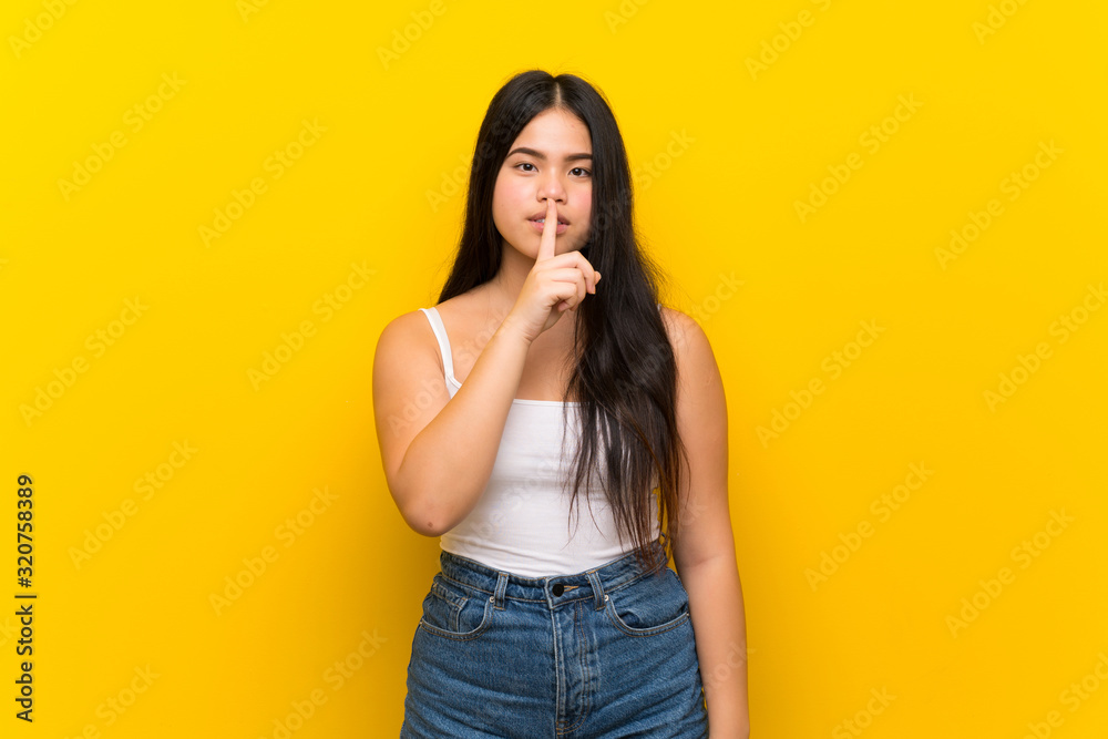 Young teenager Asian girl over isolated yellow background showing a sign of silence gesture putting finger in mouth Young teenager Asian girl over isolated yellow background showing a sign of silence gesture putting finger in mouth