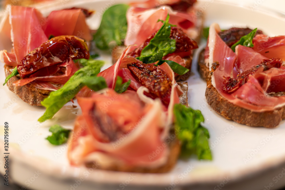 Sandwiches with prosciutto and sun-dried tomatoes on dark bread, spread with goat cheese. On a wooden background.