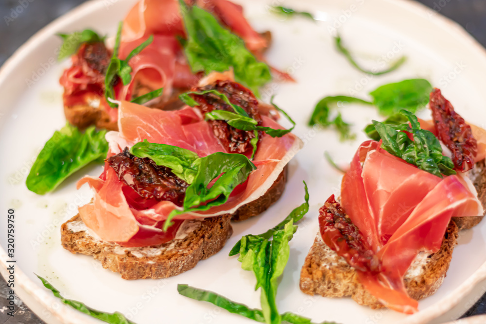 Sandwiches with prosciutto and sun-dried tomatoes on dark bread, spread with goat cheese. On a wooden background.