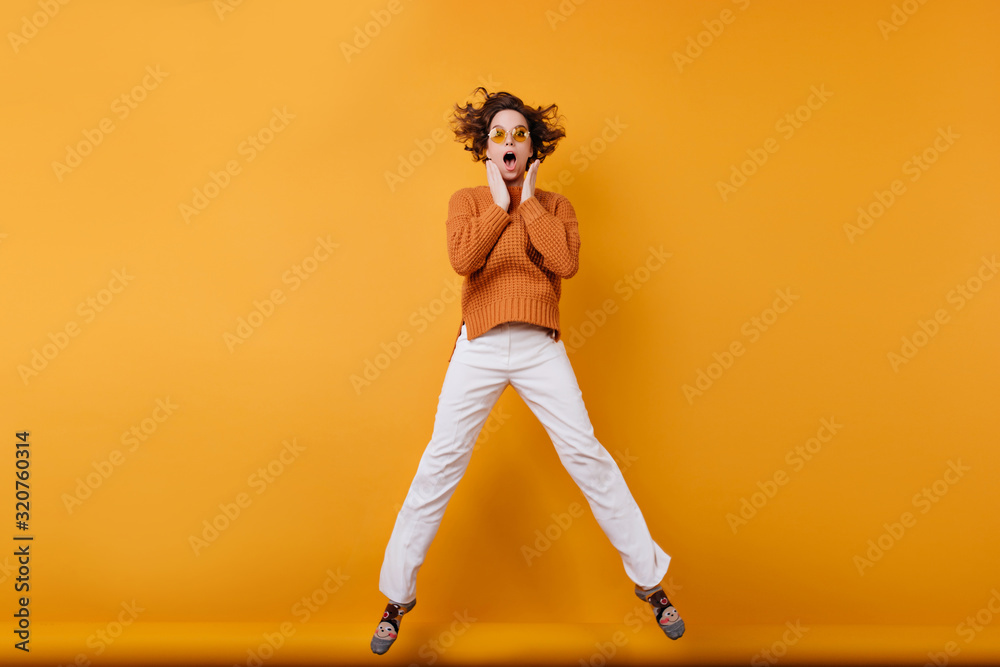 Full-length photo of amazed young woman in white pants dancing in studio. Portrait of wonderful girl with wavy hair jumping with funny face expression. Full-length photo of amazed young woman in white pants dancing in studio. Portrait of wonderful girl with wavy hair jumping with funny face expression.