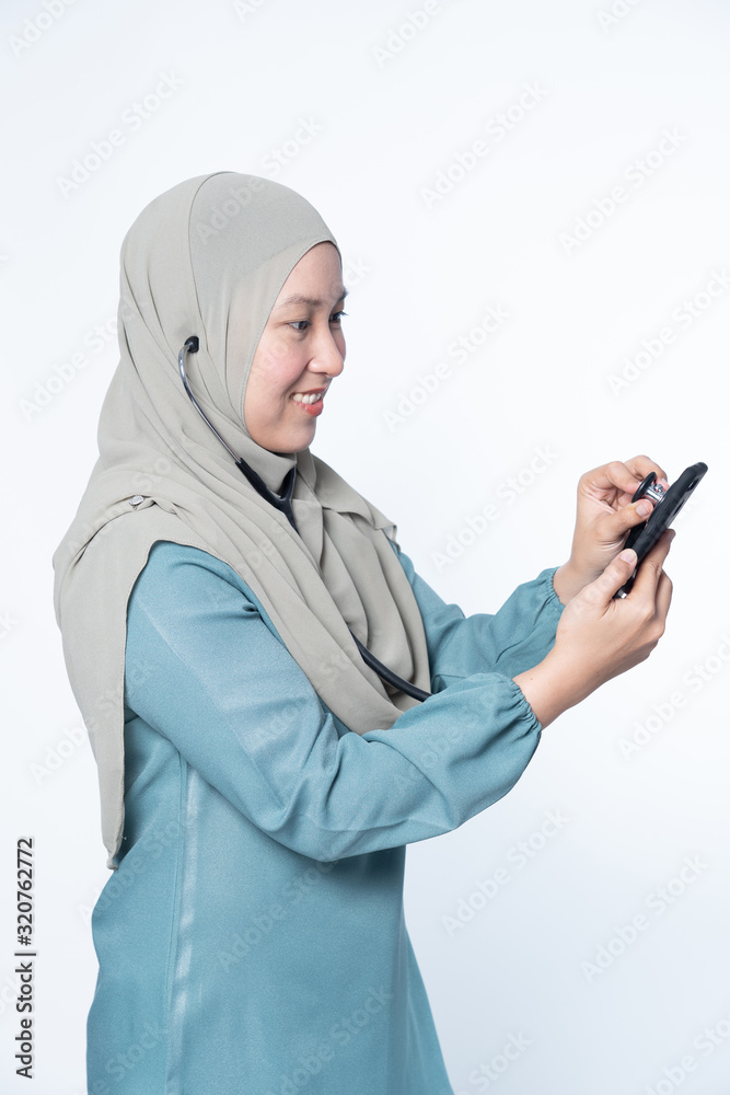 Muslim woman holding a stethoscope while inspecting a mobile phone. Muslim woman holding a stethoscope while inspecting a mobile phone.