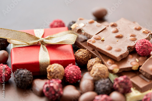 sweets, confectionery and food concept - close up of different chocolate bars, candies and gift box on brown background