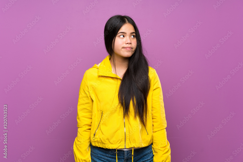 Young teenager Asian girl over isolated purple background making doubts gesture looking side Young teenager Asian girl over isolated purple background making doubts gesture looking side