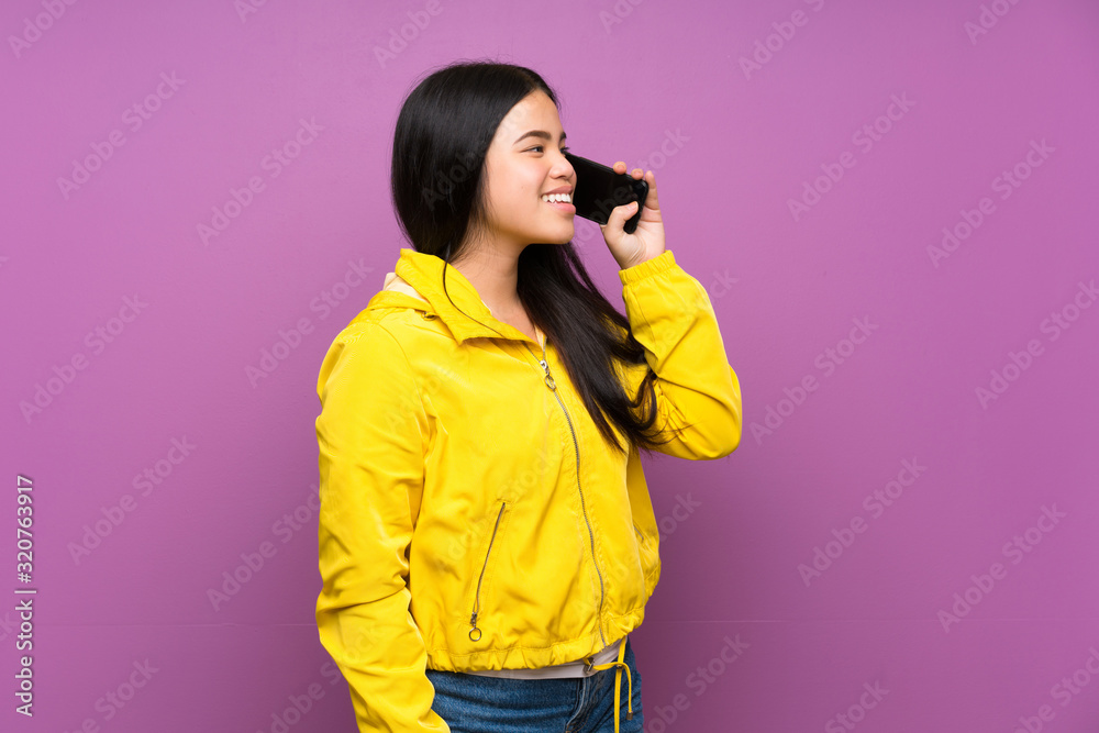 Fototapeta premium Young teenager Asian girl over isolated purple background keeping a conversation with the mobile phone