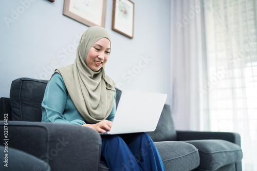 Female muslim using laptop at home environment.