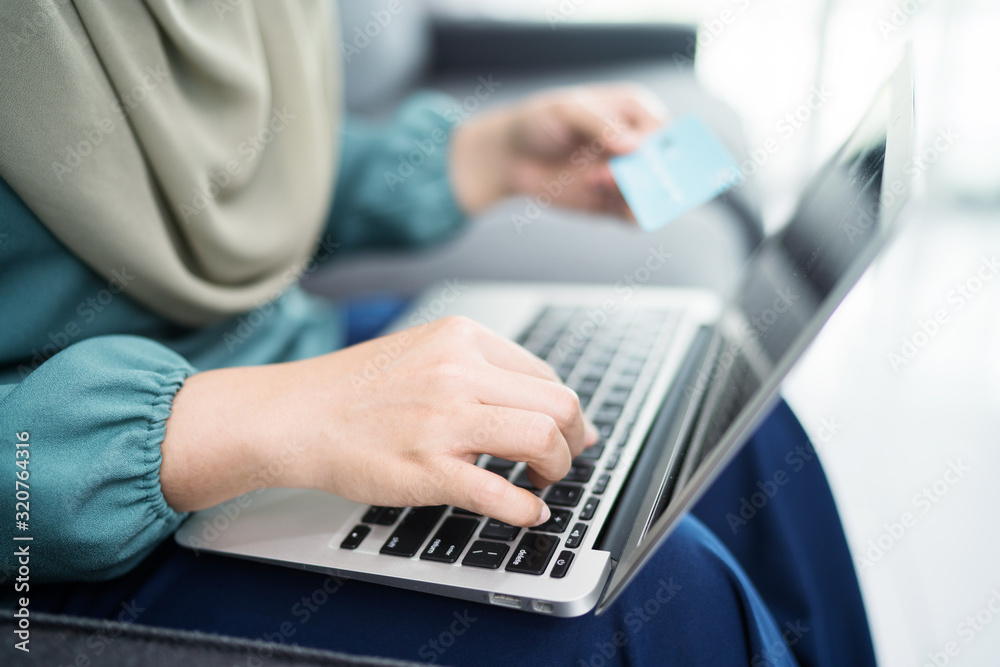 Female muslim woman using laptop while holding credit card.