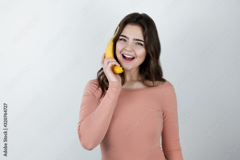 young beautiful woman holding fresh banana like a phone looking happy being on diet isolated white background young beautiful woman holding fresh banana like a phone looking happy being on diet isolated white background