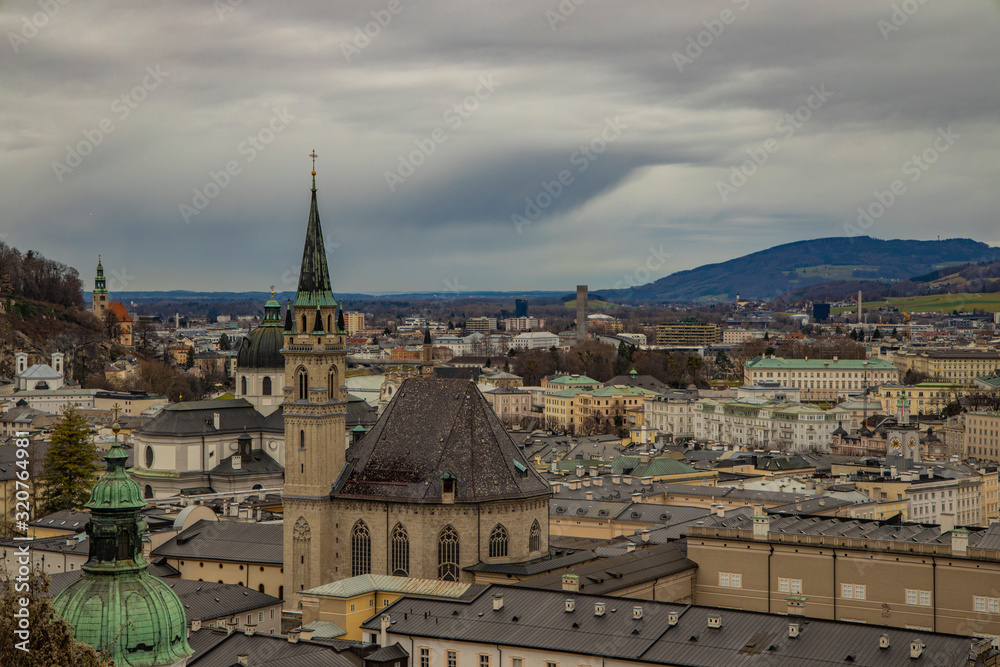 Obraz premium Salzburg old European city top view landmark heritage touristic site for visiting and sightseeing medieval houses roofs and cathedral building tower in moody weather time gray cloudy sky background