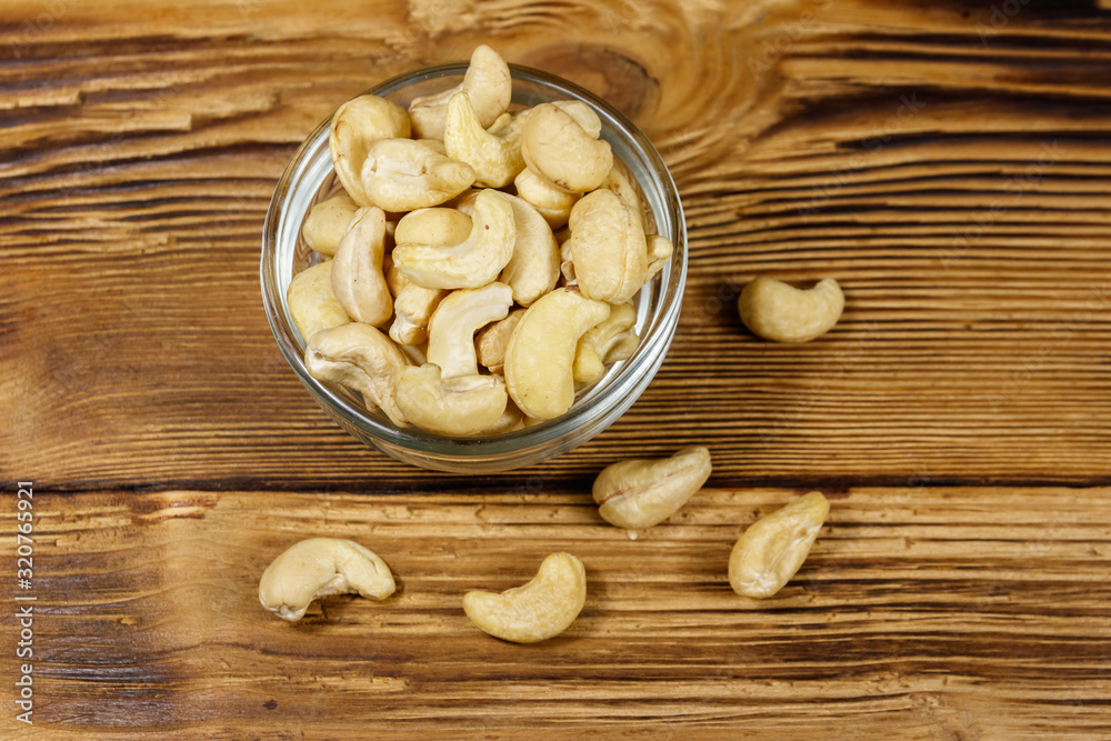 Glass bowl with raw cashew nuts on a wooden table. Top view
