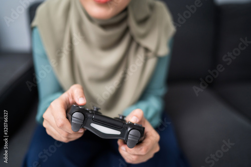 Beautiful muslim woman playing console games at her couch.
