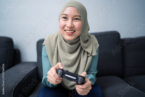 Beautiful muslim woman playing console games at her couch.