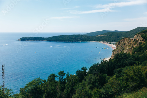 view of the sea bay with a long beach and lots of green trees around © Ksenia