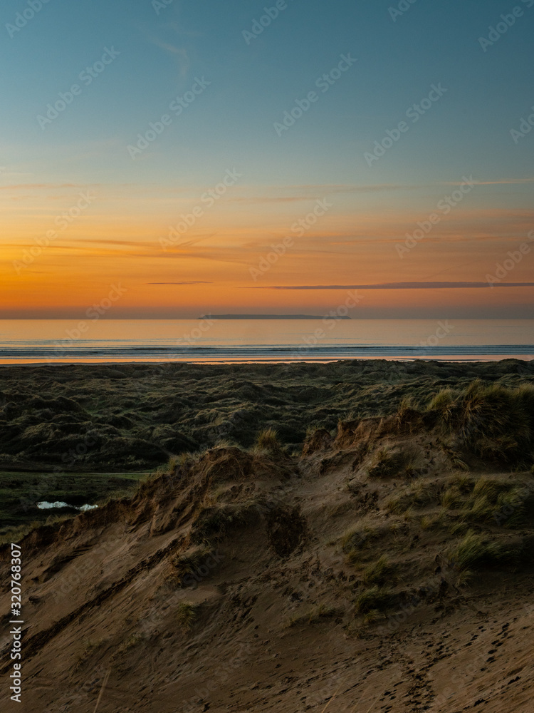 Sunset over an Island in the distance. Taken on a sand dune with beach and sea. Beautiful orange sky. Tranquil Sunset. 
