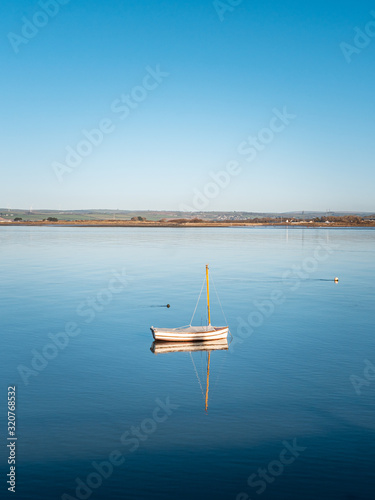 Small white fishing boat in the estuary on a very calm still day. Blue sky. Nice reflections on the water.  photo