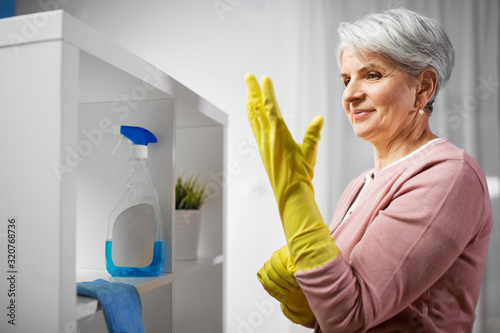 cleaning, housework and housekeeping concept - senior woman putting protective rubber gloves on at home