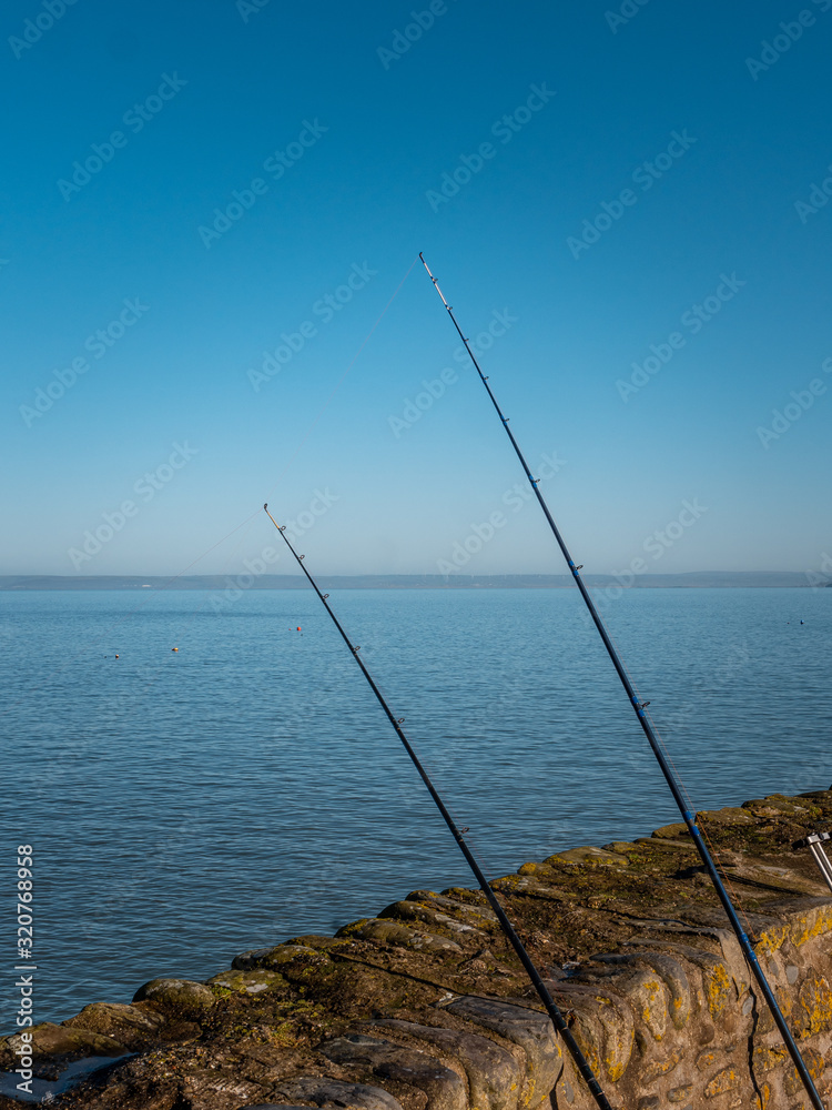 Fishing Poles leaning against a wall by the sea. 