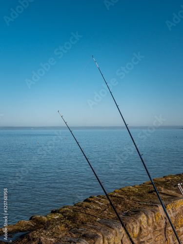 Fishing Poles leaning against a wall by the sea. 