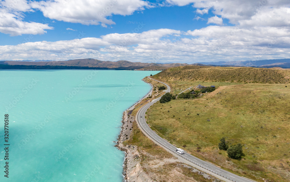 Stunning aerial high angle drone view of State Highway 8 leading along the shores of Lake Pukaki, an alpine lake on New Zealand's South Island. The water is famous for its distinct bright colour.