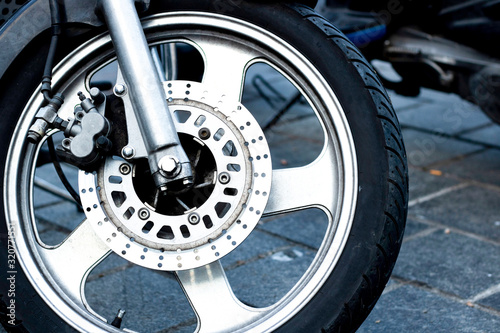 Closeup detail of a racing motorcycle's front wheel. This is the brake caliper, rotor, rim, tire, and suspension. Close up.