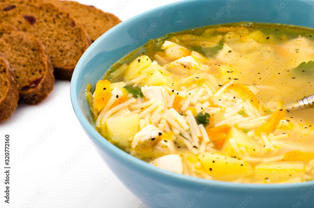 Chicken soup with vegetables in a blue plate on a white table, near a spoon and bread, closeup Chicken soup with vegetables in a blue plate on a white table, near a spoon and bread, closeup