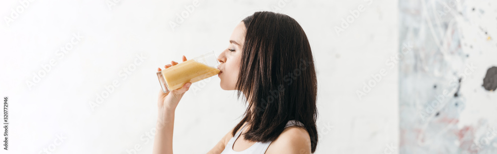 Side view of beautiful girl drinking smoothie in kitchen, panoramic shot Side view of beautiful girl drinking smoothie in kitchen, panoramic shot