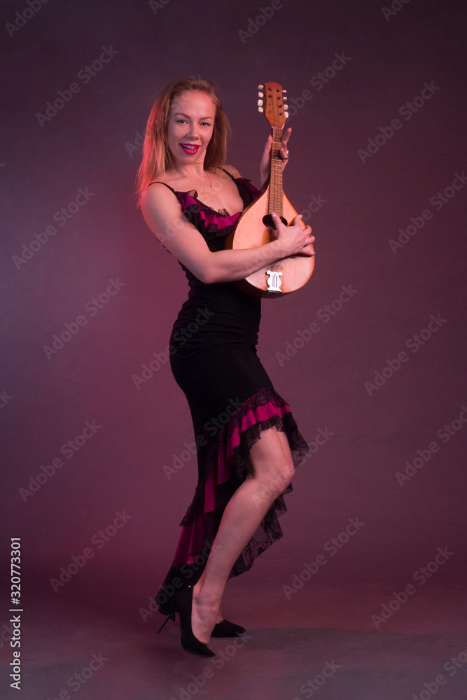 Blonde, in black dress with red flounces, with a mandolin in her hands on a Burgundy background of the Studio