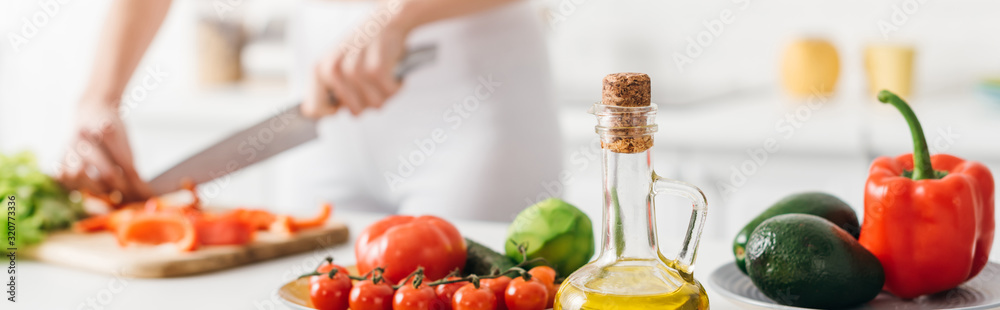 Selective focus of olive oil and fresh vegetables near woman cooking salad on kitchen table, panoramic shot - obrazy, fototapety, plakaty 