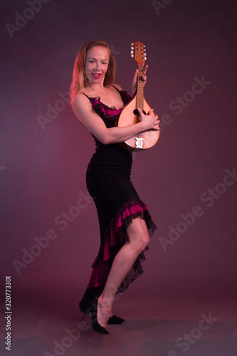 Obraz na płótnie Blonde, in black dress with red flounces, with a mandolin in her hands on a Burgundy background of the Studio w salonie