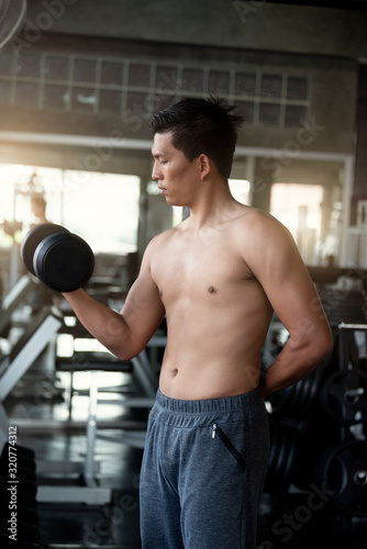 Young asian man lifting dumbbells in gym. healthy lifestyle and workout motivation concept.