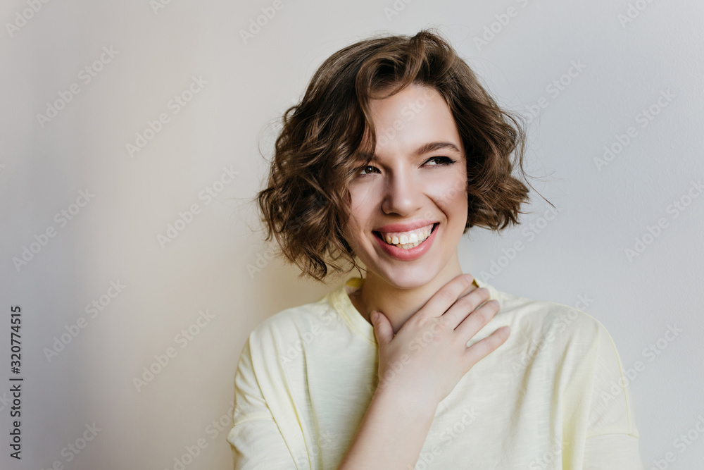 Fashionable girl with dark shiny hair looking away with happy smile. Indoor photo of enthusiastic white woman isolated on light background. Fashionable girl with dark shiny hair looking away with happy smile. Indoor photo of enthusiastic white woman isolated on light background.