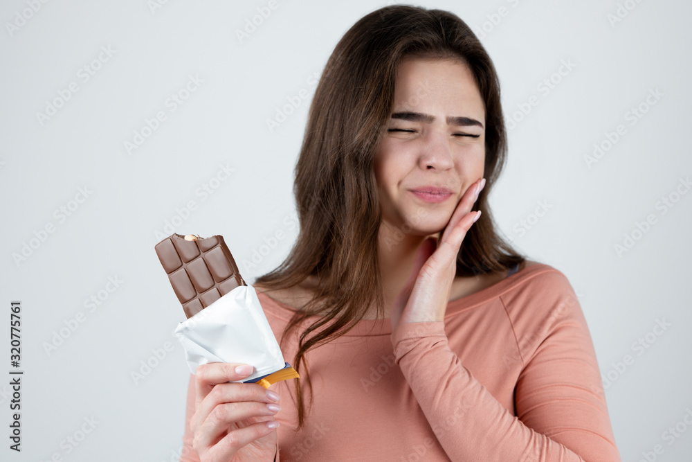 young beautiful woman suffering toothache after eating chocolate bar looking miserable standing on isolated white background, healthy lifestyle young beautiful woman suffering toothache after eating chocolate bar looking miserable standing on isolated white background, healthy lifestyle