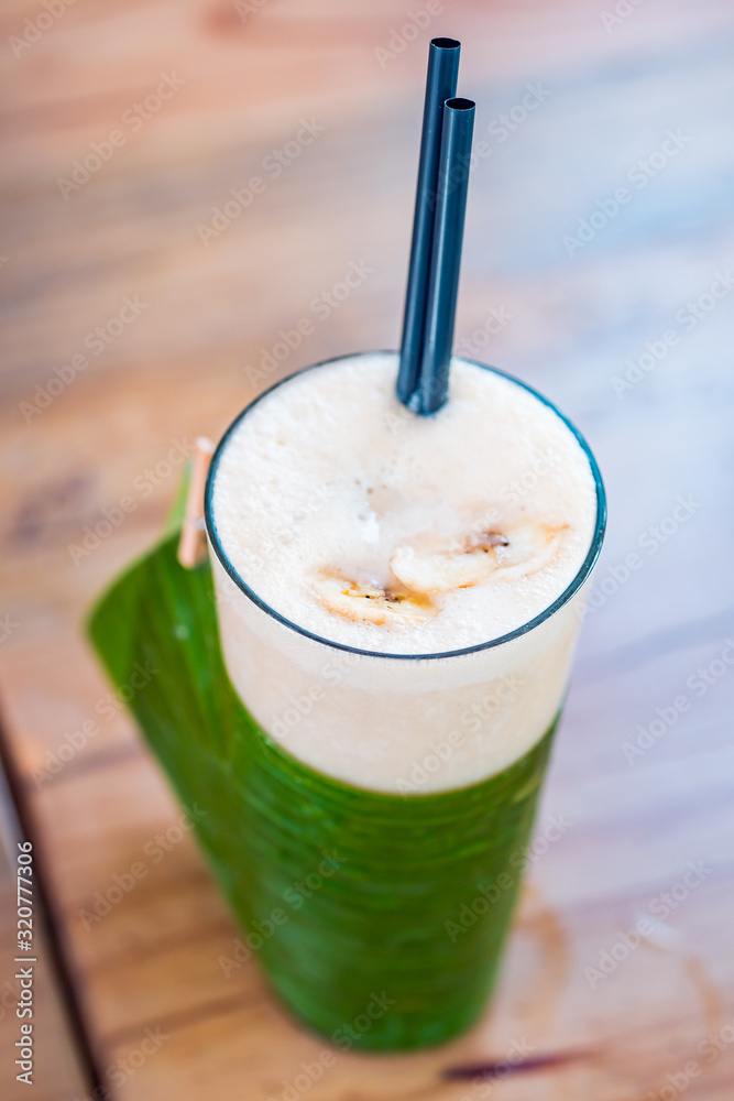 Close-up of banana milk smoothie with drinking straws served in a tall glass. Close-up of banana milk smoothie with drinking straws served in a tall glass.