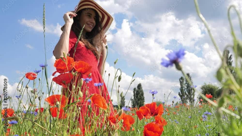 Happy young woman in red dress and big hat Enjoying Nature. Beauty Girl Outdoor walks on a poppy field. Freedom concept. Beauty Girl over Sky and Sun