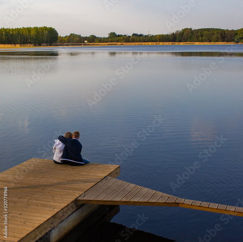 A romatic young couple - the guy and the girl sit hugged on a wooden dock in the lake. Romantic meeting.
