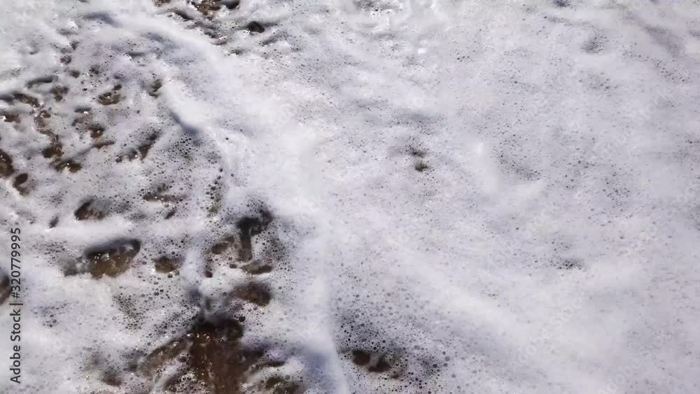Slow motion video. A white foamy wave runs onto a golden sandy shore. Travel concept. Top view, viewing point of a person standing on a sandy beach. Slow motion video. A white foamy wave runs onto a golden sandy shore. Travel concept. Top view, viewing point of a person standing on a sandy beach.